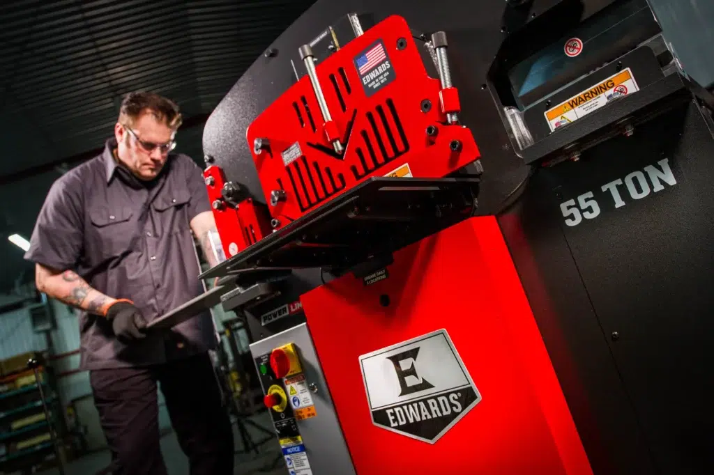 A man operates a hydraulic Edwards ironworker machine in a factory, showcasing metal fabrication processes.